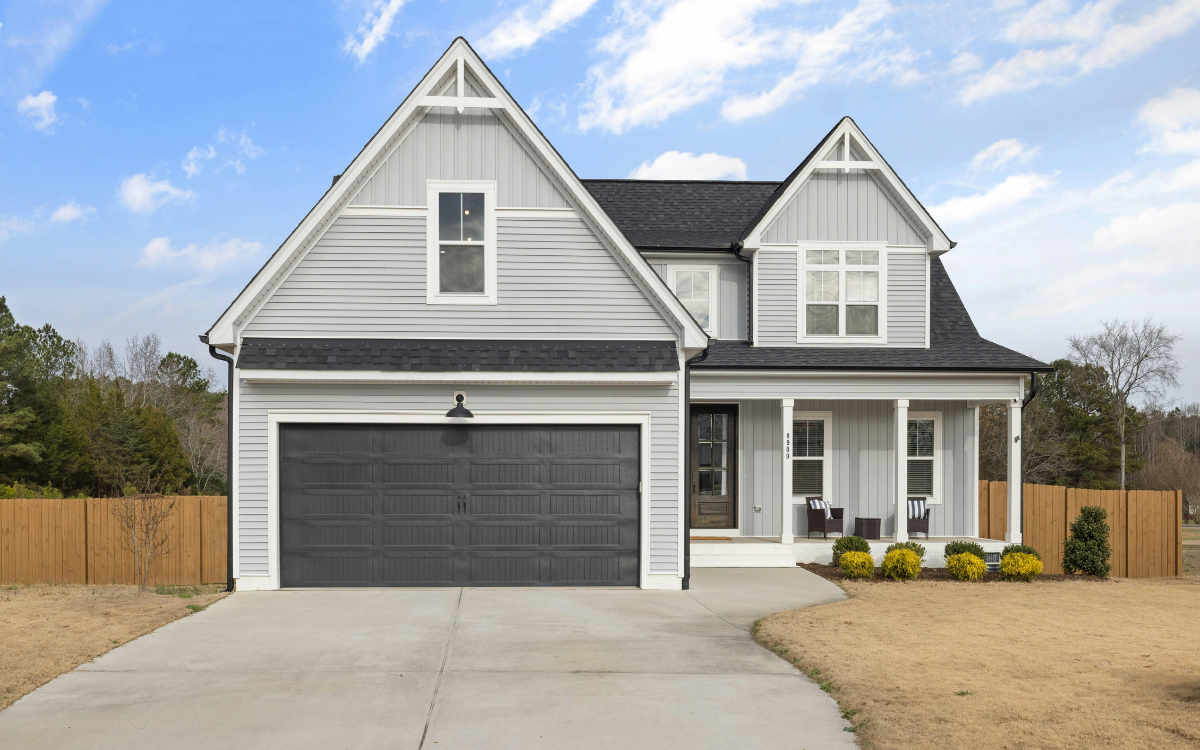 licensed-home-inspectors-northwest-arkansas - Arkansas Home Tech Inspections Two-story gray suburban house with a white garage door and a colorful front garden under a clear blue sky
